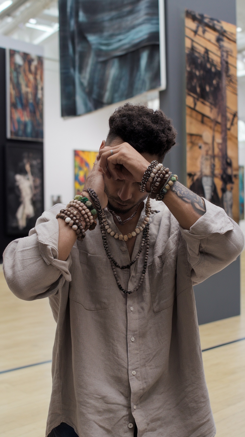 A fashionable man with layered necklaces and bracelets in an art gallery.